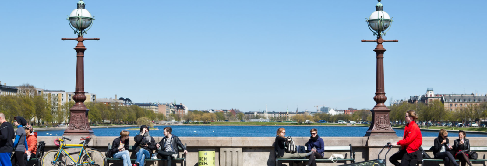 People sitting on the benches on Dronning Louise's Bridge and enjoying the sun, while a Christiania bike rides past